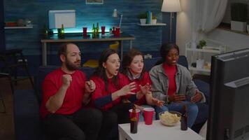 Mixed race group of people watching at football game on television cheering sport team after winning championship. Excited friends celebrating match competition while sitting on sofa late at night video