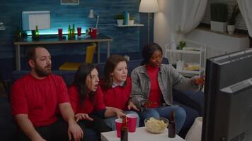 Multi ethnic friends sitting in front of television on couch while watching football competition. Multiethnic group celebrating winning of soocer match while sitting on sofa late at night video