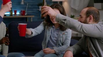 Group of multi-cultural happy friends having fun during free wekeend party drinking beer, eating snack while resting on couch. Mixed race people hanging out enjoying time spending together video