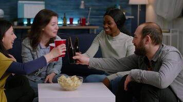 Multi ethnic friends enjoying time spend together relaxing on couch during home party. Group of multi-ethnic people hanging out, socializing during wekeend party late at night in living room video