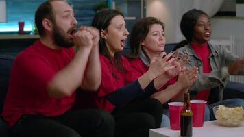 Exicited multi-ethnic friends group cheering together after foottball team winning match competition. Support team watching soccer on television late at night while sitting on sofa in living room video