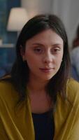 Vertical . Close up of beautiful woman looking into camera while sitting on sofa during night party. Group of multiethnic people drinking beer and talking having fun while celebrating friendship video