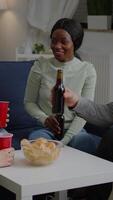 Vertical . Multi-ethnic friends spending time together, drinking beer during nightlife party while sitting on sofa late at night in living room. Group of mixed race people hanging out, having fun conversation video
