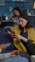 Vertical . Multiracial friends relaxing on couch while surfing news on internet using mobile speding time together during surprise party. Group of multi-ethnic people watching online funny movie in living room video