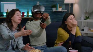 Mixed group of friends guiding afro american woman with virtual reality headset playing simulation game using controller. Afro caucasian female losing online videogame competition video