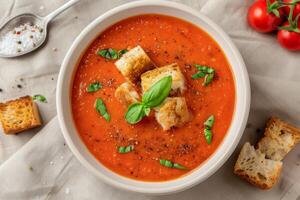 Fresh Tomato Soup With Crispy Croutons and Basil on a Light Cloth Background photo