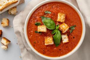 Fresh Tomato Soup With Crispy Croutons and Basil on a Light Cloth Background photo