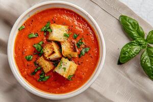 Fresh Tomato Soup With Crispy Croutons and Basil on a Light Cloth Background photo
