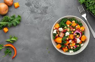 Colorful Kale Salad With Butternut Squash, Bacon, and Pine Nuts on Gray Table photo