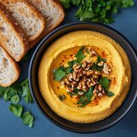 Creamy pumpkin soup topped with walnuts and fresh herbs served with slices of bread photo