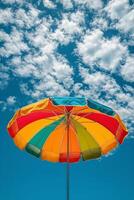 Colorful beach umbrella under a bright blue sky with fluffy white clouds photo