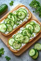 Fresh cucumber slices on creamy cheese toast stacked on a wooden cutting board photo