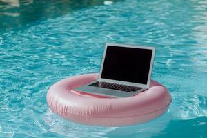 A sleek laptop on a vibrant pink pool float symbolizes work and leisure, ideal for those seeking a refreshing summer break while enjoying the sun, combining productivity and relaxation photo