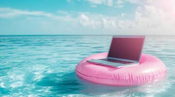 A laptop is precariously perched on a bright pink pool float, gently bobbing in the vast ocean, representing the perfect blend of work and relaxation that many modern workaholics seek photo