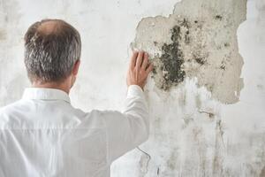 A man in a white shirt touches a moldy wall, symbolizing the need to address home maintenance issues and underscoring the importance of regular upkeep for a safe, healthy living environment photo