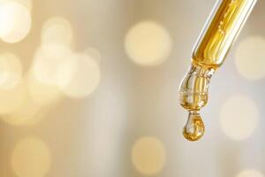A detailed closeup image shows a pipette elegantly dropping a golden serum against a beautifully shimmering background photo