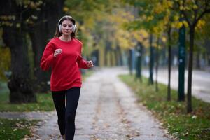 Young beautiful woman running in autumn park and listening to music with headphones on smartphone photo