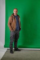 Middle aged bald man in casual attireposes confidently against a green studio backdrop. photo