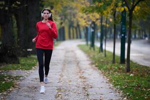 Young beautiful woman running in autumn park and listening to music with headphones on smartphone photo