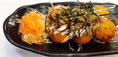 Close up Takoyaki with carrot, cabbage sliced and dried seaweed on black plate at Japanese restaurant. Fried and Asian food. photo