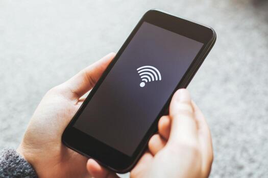 Hand holding smartphone with glowing wifi icon on screen, background photo