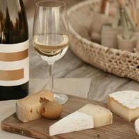 A cozy wine and cheese tasting setup, featuring a glass of white wine with assorted cheeses on a wooden board. photo