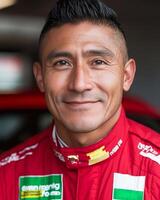 Close-up of smiling race car driver in red uniform with sponsorship logos against blurred racing car background. photo
