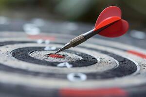 Closeup of red dart hitting bullseye on target board, blurred background. Conceptual photo for goal setting and success in business or sports