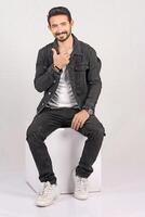 Portrait of a young stylish male model in black jeans jacket and pant with smile full height and sitting studio shots photo