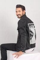 Portrait of a young stylish male model in black jeans jacket and pant with smile full height and sitting studio shots photo