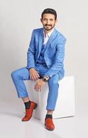 Portrait of a young stylish beard bussiness man in blue suit with smile full height and sitting studio shots photo