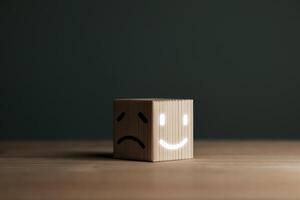 A smiling face on bright side and sad face on dark side of wooden block. Concept business for satisfaction assessment and mental health concepts for positive thinking and emotional states. photo