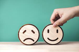 Evaluation level and measurement of quality of customer service. Hand picked wooden circle with most satisfied smiley emoji on green background. photo