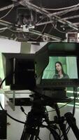 Vertical portrait of camerawoman operating professional camera on rig with female director giving instruction. Professional filming pavilion. TV presenter behind the scene video