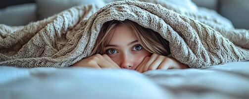Girl lying in bed with the blanket pulled over her head, only her hands peeking out, playful and hidden photo