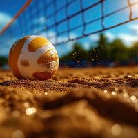 A close-up view of a volleyball resting on sandy court with a net overhead and sun shining in the background. photo