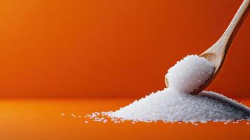 A close-up of granulated sugar being scooped with a wooden spoon against a vibrant orange background, showcasing texture and color. photo