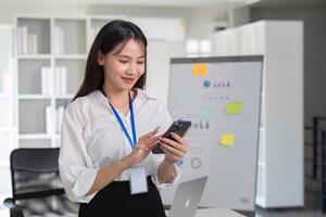 Young Accountant Using Smartphone in Modern Office Setting with Charts and Laptop in Background photo