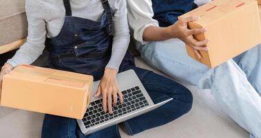 Couple Checking Merchandise Boxes for Online Delivery While Using Laptop for E-commerce Business photo