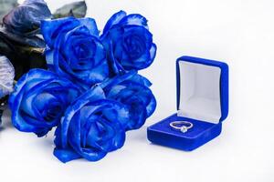 Golden engagement ring in a blue velvet box and blue rose shallow DOF photo