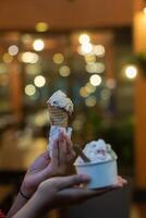 Close up hand of a person holding a cup and a cone of ice cream with blurred background photo