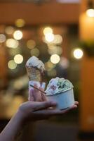 Close up hand of a person holding a cup and a cone of ice cream with blurred background photo