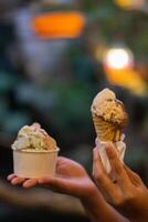 Close up hand of a person holding a cup and a cone of ice cream with blurred background photo