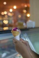 Close up hand of a person holding a cone of ice cream with blurred background photo