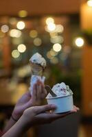 Close up hand of a person holding a cup and a cone of ice cream with blurred background photo