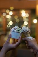 Close up hand of a person holding a cup and a cone of ice cream with blurred background photo
