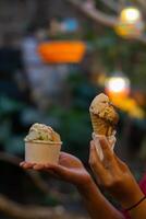 Close up hand of a person holding a cup and a cone of ice cream with blurred background photo