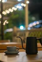 Cup of coffee and teapot on the table with blurred background photo