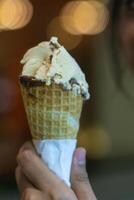 Close up hand of a person holding a cone of ice cream with blurred background photo