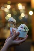 Close up hand of a person holding a cup and a cone of ice cream with blurred background photo